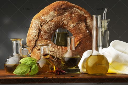 عکس با کیفیت یک نان بزرگ در کنار شیشه های روغن روی میز چوبی