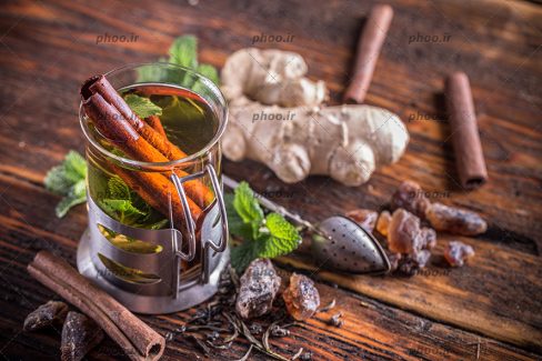 عکس با کیفیت یک فنجان چای گیاهی با نعناع تازه و زنجبیل روی میز چوبی