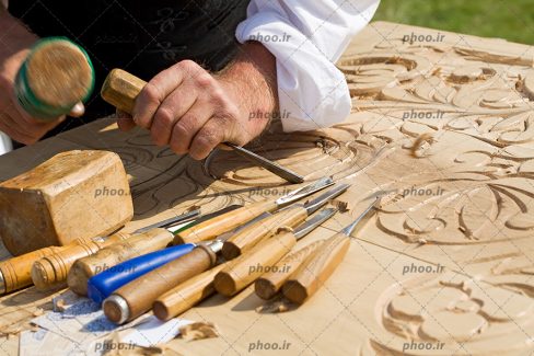 عکس نجار هنرمند در حال کنده کاری سنتی با نقوش گل روی چوب