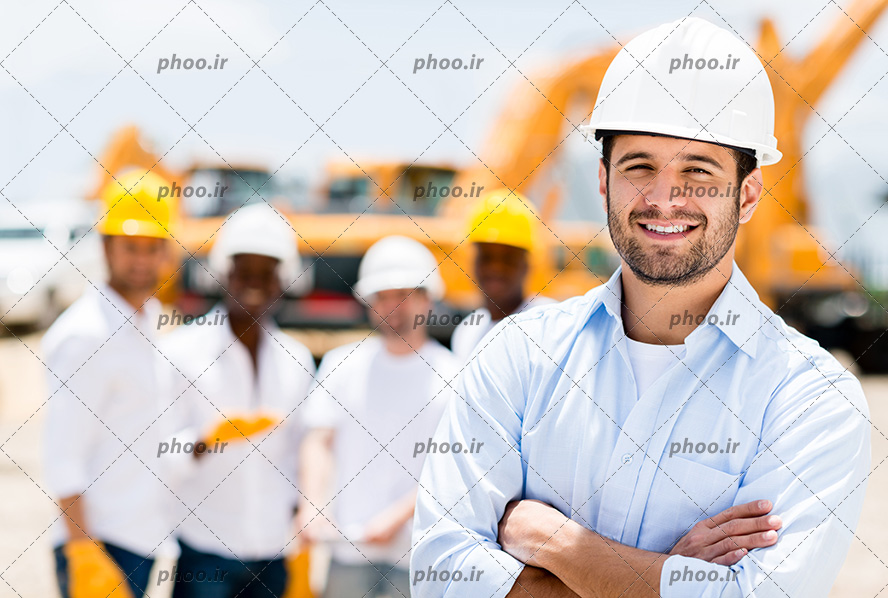 عکس مهندس با کلاه ایمنی و ایستاده با ژست و در حال لبخند زدن و چند مهندس ساختمان ایستاده در پشت سرش