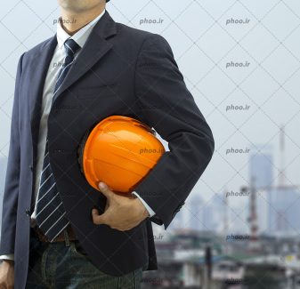 عکس مهندس با کت شلوار و کلاه ایمنی در پس زمینه شهر