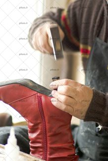 عکس کفاش چکش در دست در حال تعمیر کفش در کارگاه