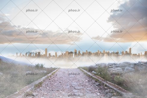 عکس با کیفیت مسیر صخره ای منتهی به شهری بزرگ در مه و زیر آسمان ابری