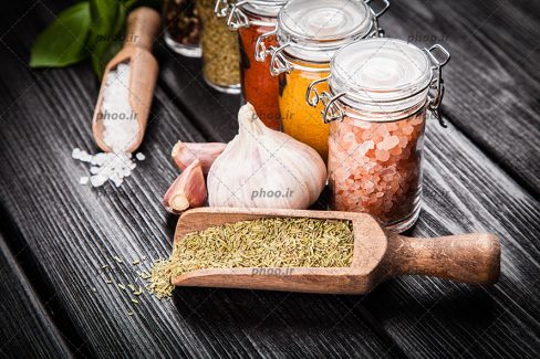 عکس ادویه هایی در ظرف های شیشه ای در پس زمینه چوب مشکی