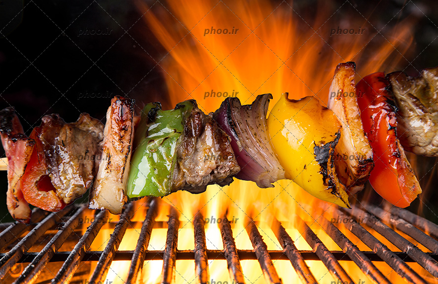 عکس گوشت و سبزیجات روی شعله آتش باربیکیو در حال کباب شدن