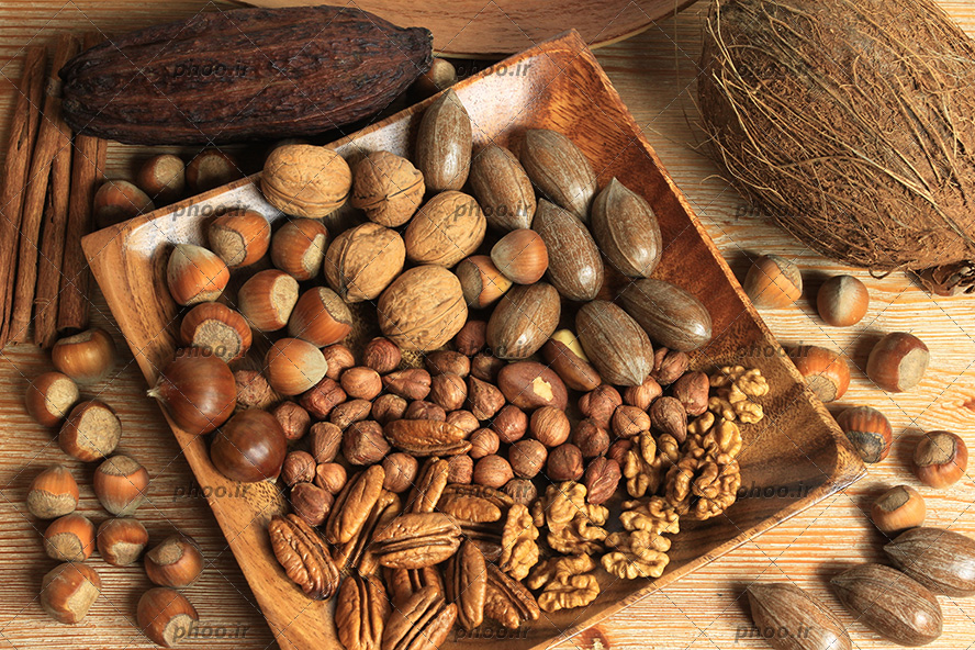 عکس با کیفیت آجیل ها و مغز هایی داخل ظرف چوبی و روی زمین