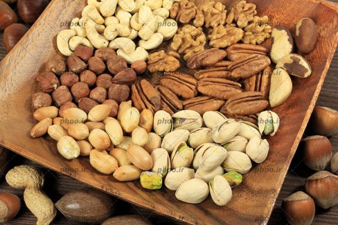 عکس با کیفیت آجیل ها و مغز هایی داخل ظرف چوبی و روی زمین