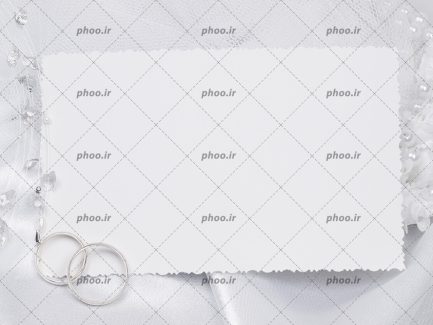 عکس با کیفیت یک کارت سفید خالی و دو حلقه ی نقره ای ازدواج روی لباس عروس