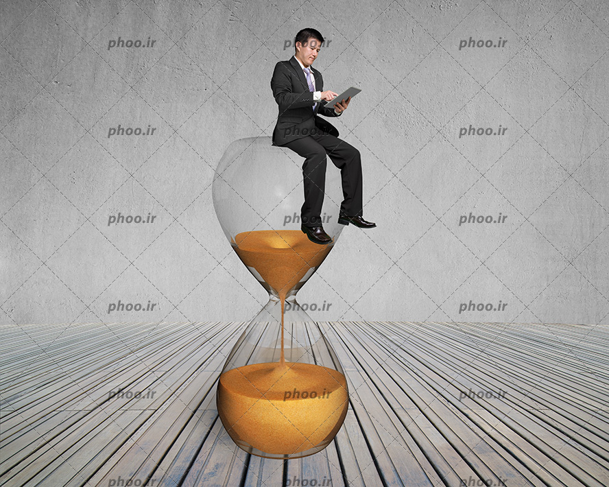 عکس مرد با یک تبلت در دست نشسته روی ساعت شنی در پس زمینه خاکستری