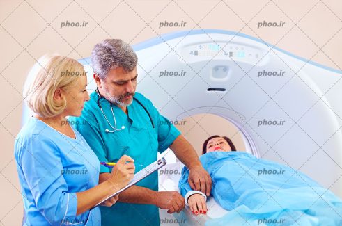عکس پزشک و پرستار در حال آماده كردن بیمار روی تخت سی تی اسکنر در بیمارستان