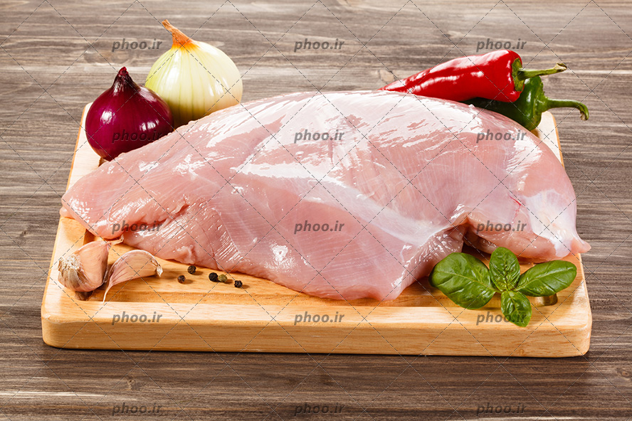 عکس فیله مرغ در کنار پیاز و گوجه و سیر روی تخته چوبی