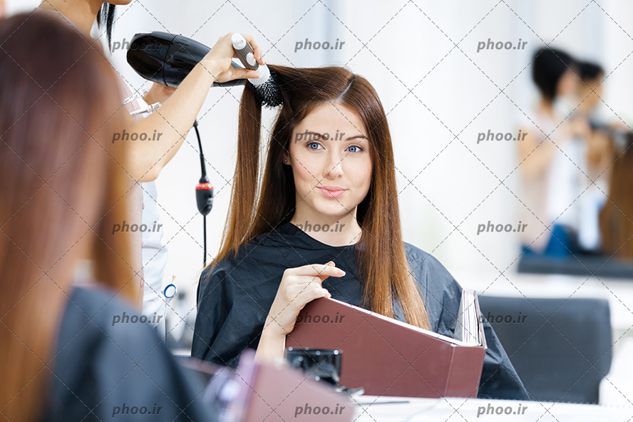 عکس خانم در آرایشگاه که آرایشگر مو هایش را سشوار می کند