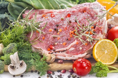 عکس گوشت خام در کنار ادویه و سبزیجات از نمای نزدیک