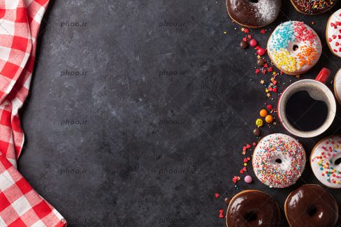 عکس دونات هایی با تزئین های متفاوت در کنار یک فنجان قهوه در پس زمینه مشکی