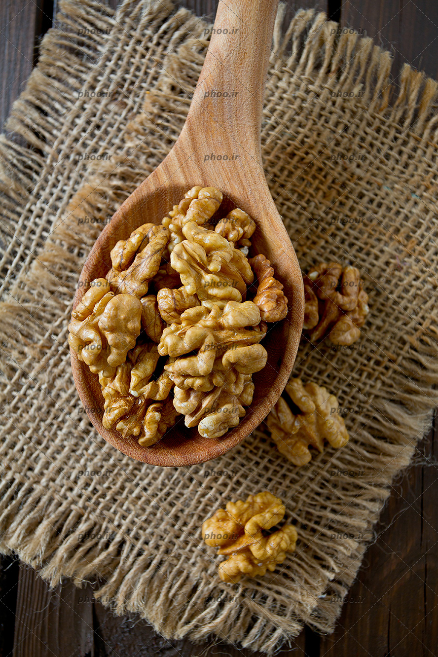عکس مغز گردو در قاشق چوبی و روی زمین در پس زمینه چوبی
