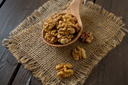 عکس مغز گردو در قاشق چوبی روی پارچه کنفی در پس زمینه چوبی