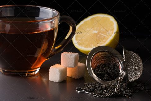 عکس صافی چای با چای خشک در کنار لیمو و قند و فنجان چای در پس زمینه مشکی