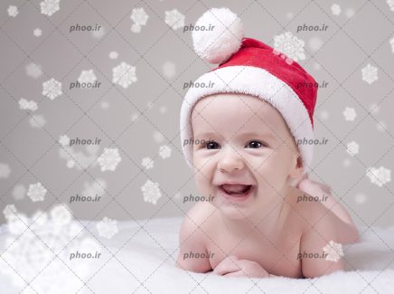 عکس با کیفیت کودک خندان با کلاه بابانوئل و دانه های برف اطراف او