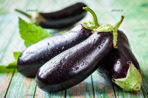 عکس بادمجان های تازه و قطرات آب روی آن ها روی میز چوبی
