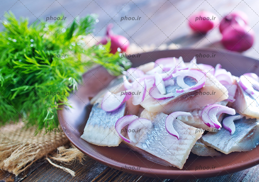 عکس ظرفی از ماهی و پیاز های چیده شده روی آن در کنار سبزی