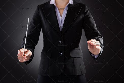 عکس رهبر گروه ارکستر باتوم به دست در پس زمینه مشکی