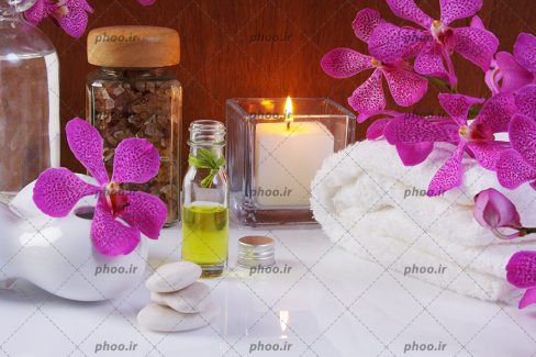 عکس زیبای روغن بدن و حوله و شمع با گل