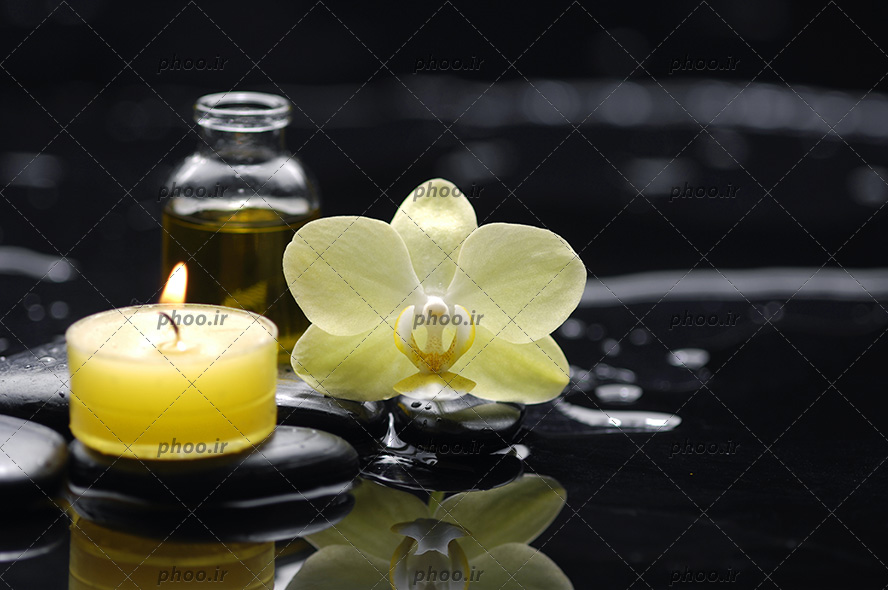 عکس زیبا بطری شیشه ای روغن ماساژ با شمع و گل و سنگ روی زمین