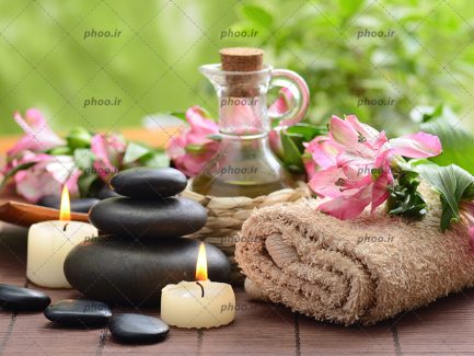 عکس زیبا بطری شیشه ای روغن ماساژ با شمع و سنگ و حوله با گل