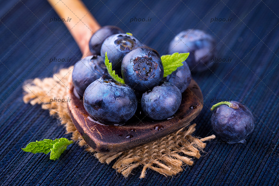 عکس بلوبری های تازه روی قاشق چوبی در پس زمینه سرمه ای