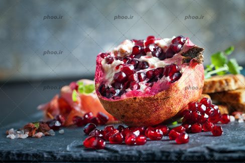 عکس انار نصف شده و دانه های قرمز آن روی زمین