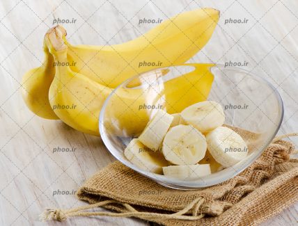 عکس موز و برش هایی از آن در کاسه شیشه ای در پس زمینه چوبی