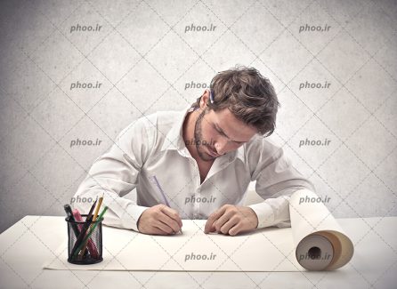 عکس با کیفیت از یک مرد جوان در حال طراحی روی کاغذ پشت میز