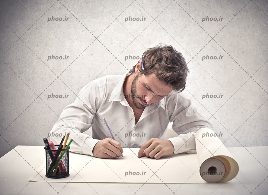 عکس با کیفیت از یک مرد جوان در حال طراحی روی کاغذ پشت میز