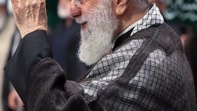 عکس با کیفیت مقام معظم رهبری ایستاده در جمعی از مردم و در حال سلام دادن با دست خود در حالت نیم رخ