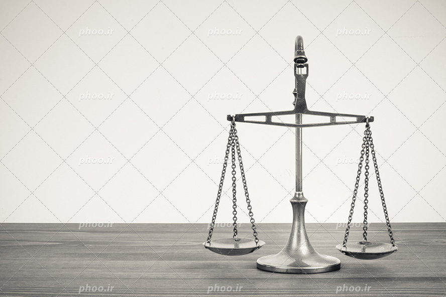 عکس با کیفیت بسیار زیبا ترازوی عدالت نقره بر روی میز چوبی در پس زمینه سفید