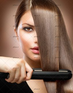 عکس خانم با آرایش و مو های قهوه ای بلند در حال اتو کردن مو