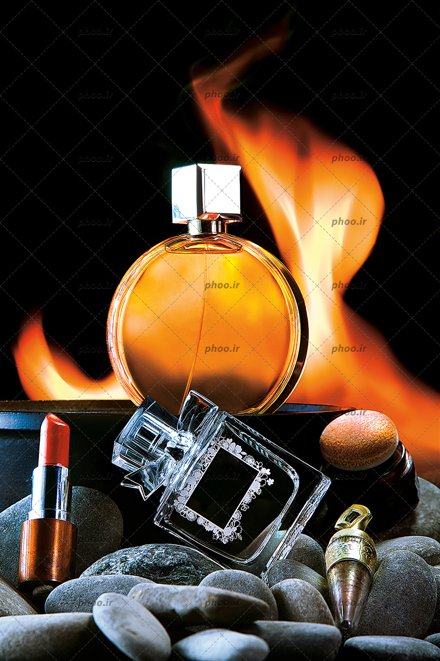 عکس دو بطری عطر زنانه و مردانه و لوازم آرایشی در برابر یک پس زمینه شعله آتش
