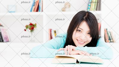 عکس دختر با لبخند در حال مطالعه در پس زمینه کتابخانه