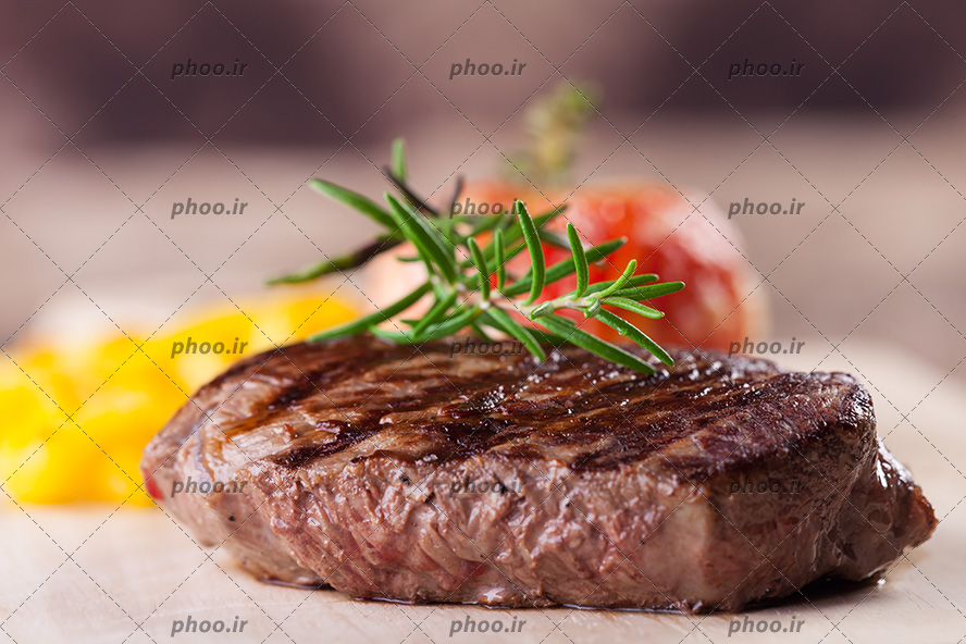 عکس استیک کبابی با تزئین سبزی روی آن روی میز چوبی