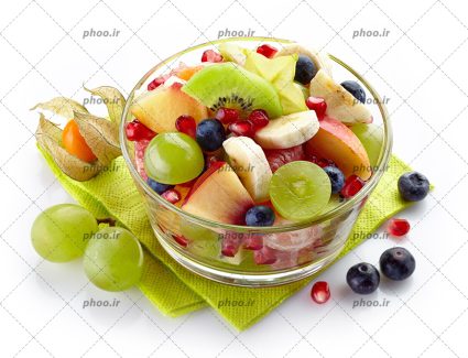 عکس کاسه شیشه ای از میوه های تازه روی دستمال سبز در پس زمینه سفید