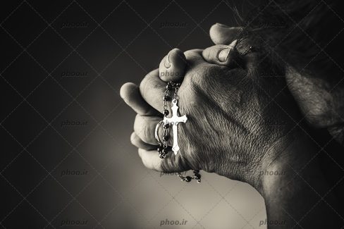 عکس دست های به هم گره خورده پیر زن در حال دعا کردن با تسبیح در تاریکی