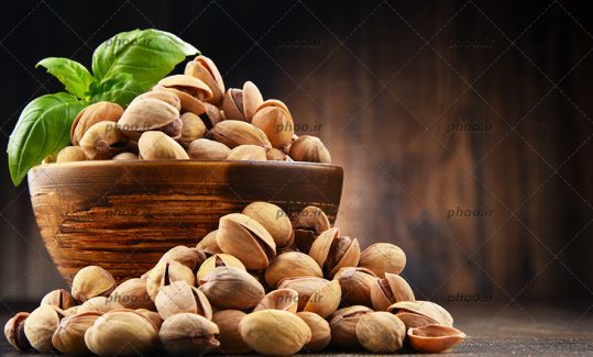 عکس پسته های خندان در کاسه و روی زمین در پی زمینه چوبی