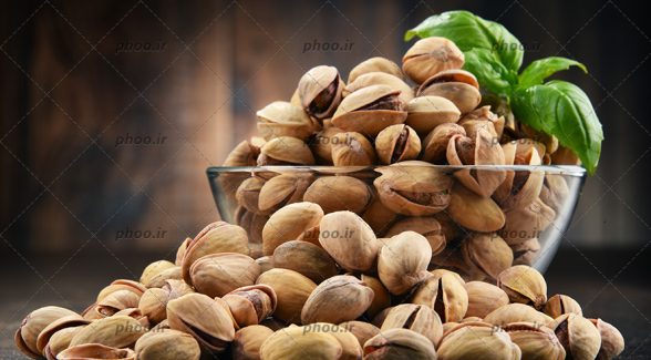 عکس پسته های خندان و برگ ریحان در کاسه و روی زمین در پس زمینه چوبی