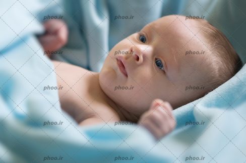 عکس با کیفیت کودک با چشم های آبی دراز کشده روی پتوی آبی