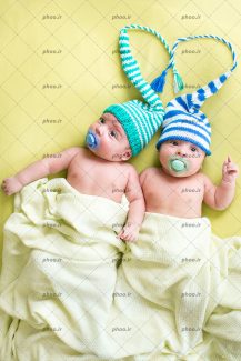 عکس با کیفیت نوزاد پسر دوقلو با کلاه راه راه با یک قلب درست شده بالای سر آن ها