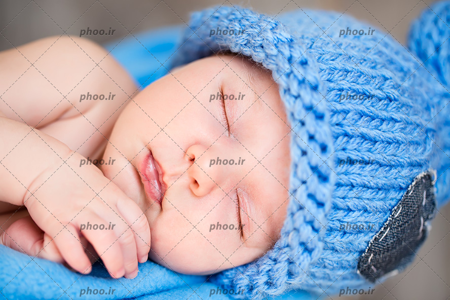 عکس با کیفیت نوزاد خوابیده با کلاه آبی بافتنی روی پتوی آبی