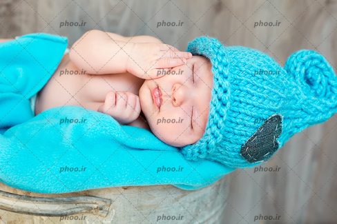 عکس با کیفیت نوزاد ناز خوابیده با کلاه آبی بافتنی روی پتوی آبی
