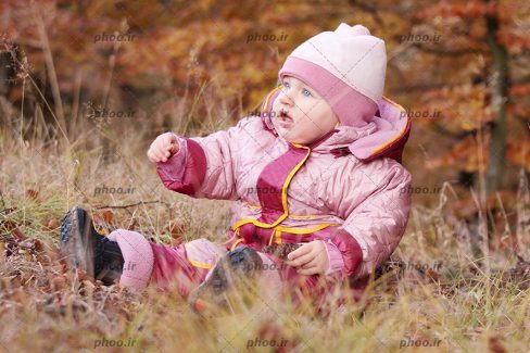 عکس با کیفیت کودک با لباس گرم نشسته در پس زمینه پاییزی