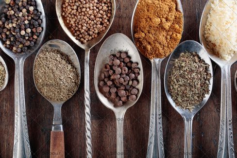 عکس قاشق هایی با ادویه های متفاوت در آن در پس زمینه چوبی