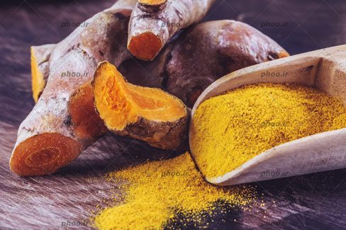 عکس زردچوبه و پودر زردچوبه در قاشق چوبی در پس زمینه چوبی